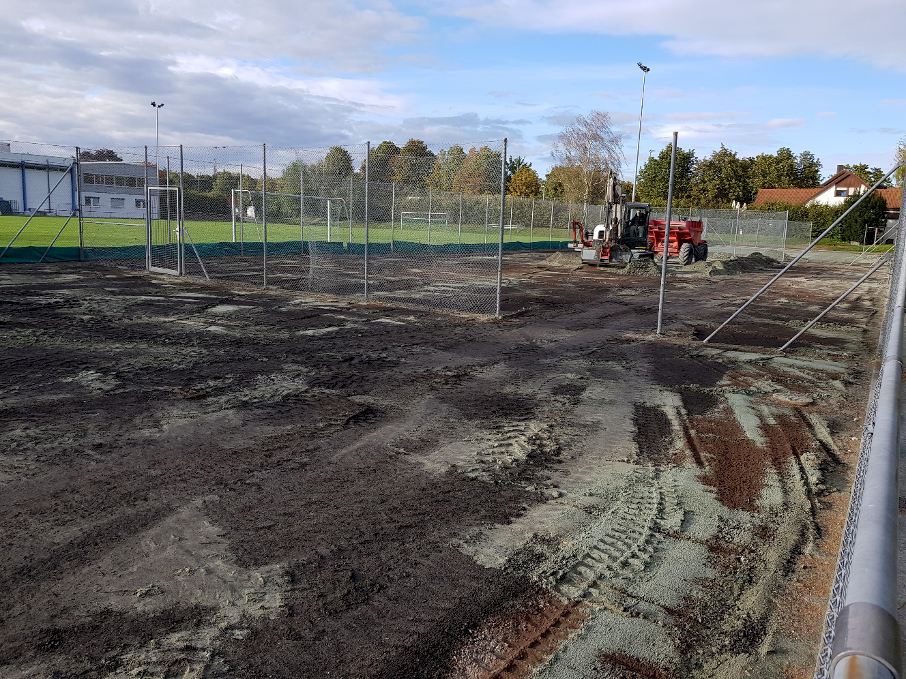 Baustelle der Tennisanlage mit Erdarbeiten und Baumaschine; im Hintergrund Gebäude und Bäume.