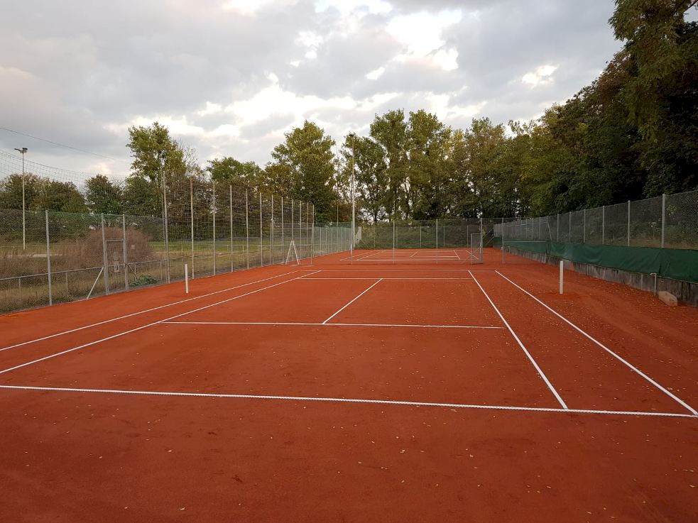 Tennisplatz mit rotem Sand und weißen Linien.
